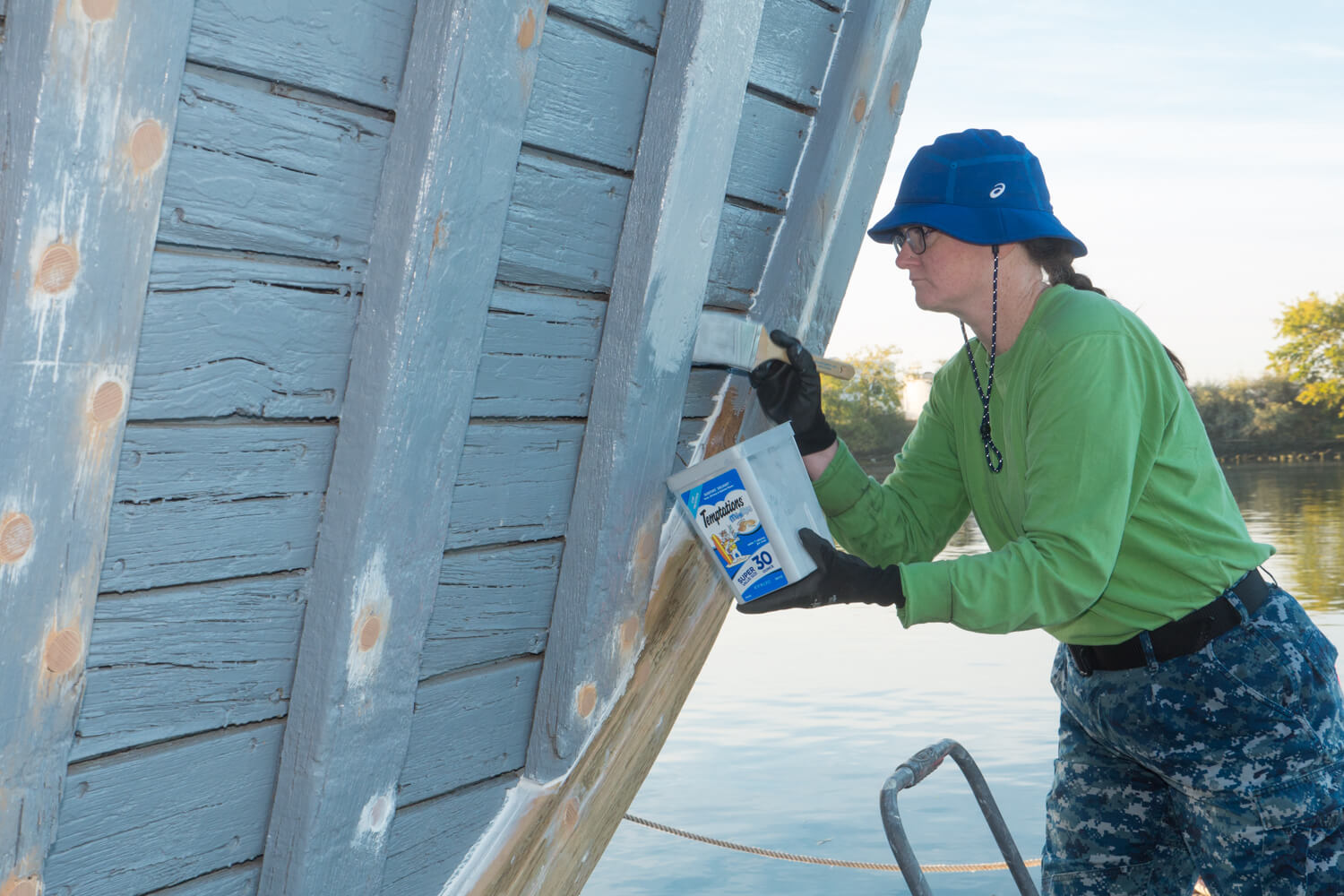 Volunteer painting the exterior wooden hull of the USS Lucid during restoration.