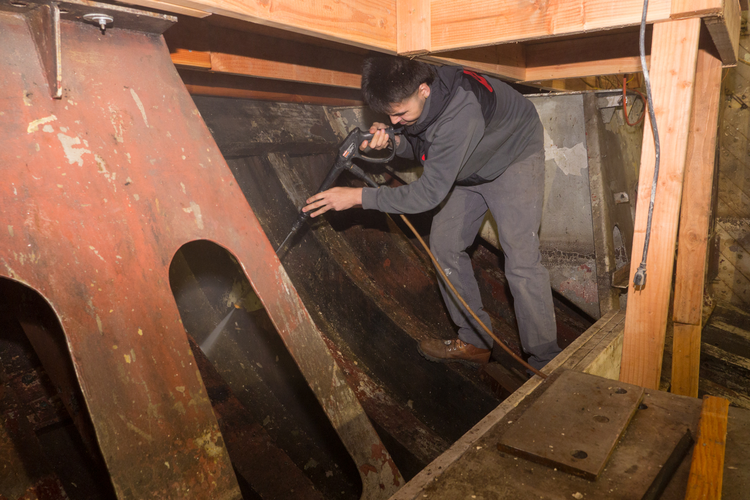 Volunteer cleaning and restoring the interior wooden hull of the USS Lucid during preservation work.